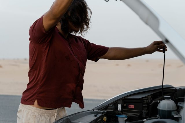 Driver stood at the open hood of a car that has broken down at the roadside