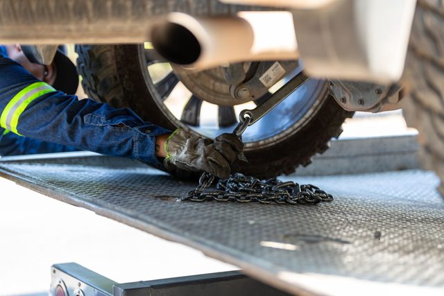 Operator in a hi-vis jacket hooking a recovery chain to a vehicle axle on a flatbed deck
